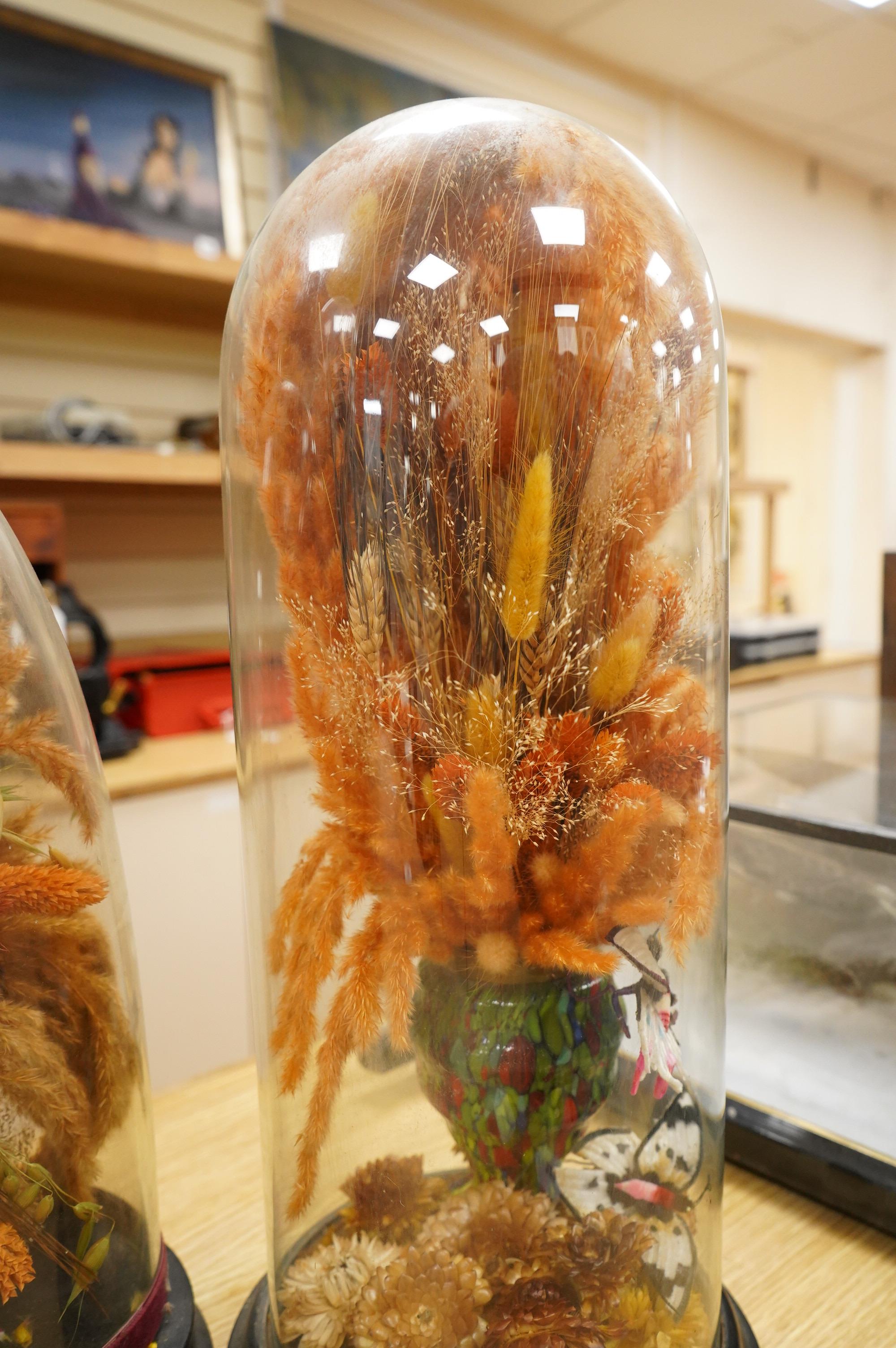 Two Victorian fauna displays under domes with ebonised bases, containing dried grasses and flowerheads, together with fabric butterflies, tallest 46cm, both af